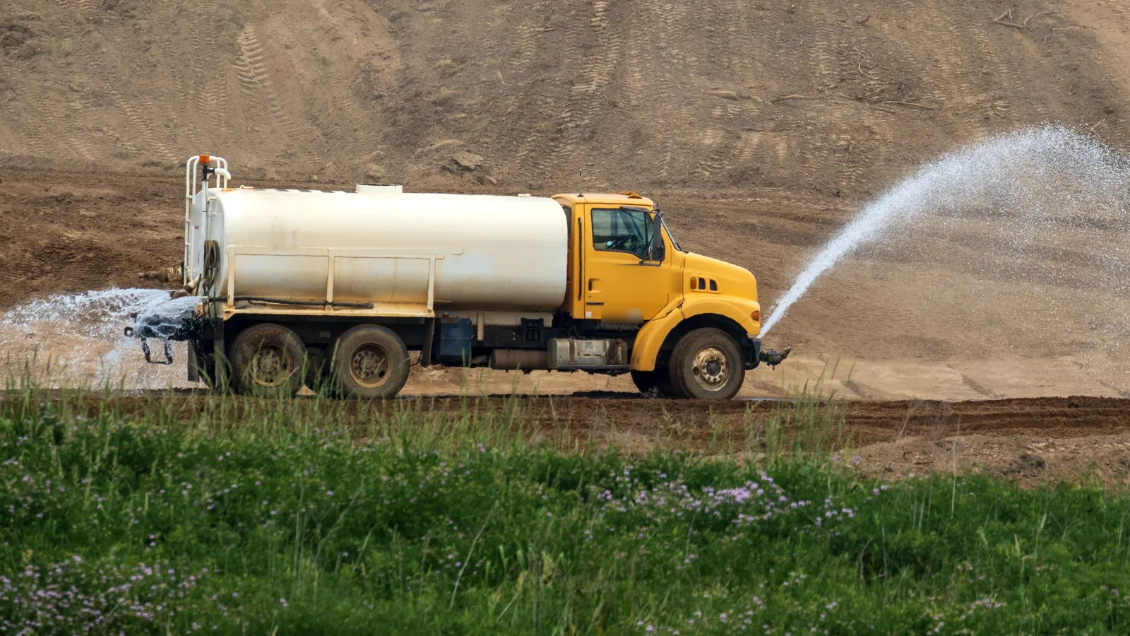 Camión cisterna amarillo rociando agua sobre el terreno de una obra